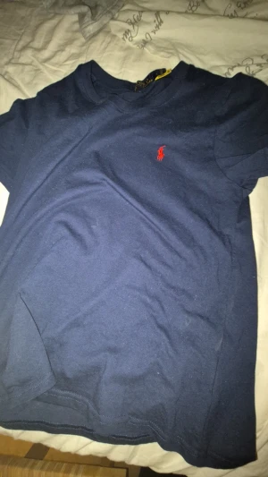 Mörkblå t-shirt från Polo Ralph Lauren - Snygg mörkblå t-shirt från Polo Ralph Lauren med klassisk röd logga broderad på bröstet. Modellen är kortärmad och har rund hals. Tillverkad i mjuk bomull som är skön mot huden. Perfekt för dig som gillar stilrena och tidlösa plagg.