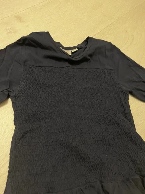 Marinblå blus med volang från Gina Tricot - Säljer en marinblå blus från Gina Tricot i storlek 158/164. Toppen har korta ärmar, smockad front och en söt volangkant längst ner. Materialet är mjukt och känns som bomull, perfekt för dig som gillar stilrena och trendiga detaljer.