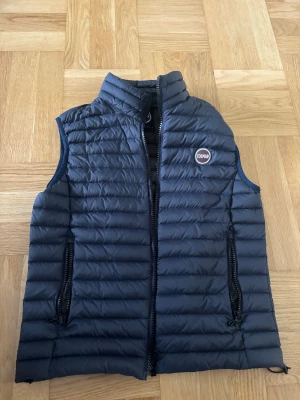 Mörkblå dunväst från Colmar - Snygg mörkblå dunväst från Colmar med quiltad design och hög krage. Västen har två praktiska fickor med dragkedja och ett diskret Colmar-märke på bröstet. Perfekt att slänga över en hoodie eller tröja när det är kyligt ute.