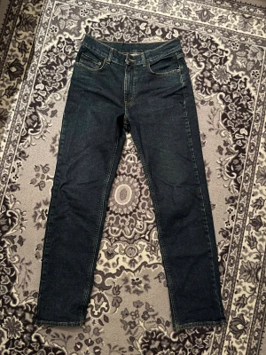 Mörkblå jeans från Mc Gordon - Säljer ett par mörkblå jeans från Mc Gordon med klassisk femficksdesign och kontrastsömmar. Modellen har raka ben och normal passform, med snygga detaljer som nitar och läderpatch bak i midjan. Perfekt för dig som gillar stilrena och tidlösa jeans. Skick 9/10 