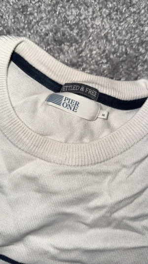 Vit randig tröja från Pier One - Snygg vit tröja från Pier One i storlek M med svarta horisontella ränder. Tröjan har rund hals, långa ärmar och ribbade muddar vid ärmslut och nederkant. Materialet är mjuk bomull som känns skönt mot huden. Perfekt för dig som gillar enkel och stilren design.