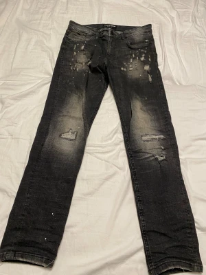 Svarta jeans från Supply & Demand  - Svarta jeans från Supply & Demand med coolt slitna detaljer partier. Dragkedja i myntfickan. Jeansen är tillverkade i denim och har en urban vibe med små färgstänk och trasiga partier.