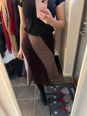 Brun och beige manchesterkjol - Snygg långkjol i manchester med breda diagonala paneler i mörkbrunt och beige. Kjolen har en lätt utsvängd form som ger en cool siluett och passar perfekt till boots. Ingen synlig dragkedja eller knappar, bara rena linjer. 