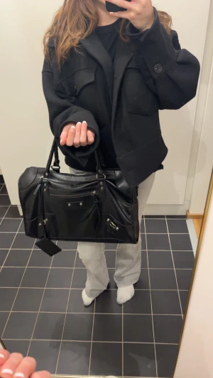 Balenciaga svart skolväska - Säljer en Balenciaga handväska i svart skinn med klassiska detaljer som silverfärgade nitar, dragkedja framtill och flätade handtag. Väskan har en rektangulär form. Perfekt storlek för att få plats med allt du behöver. Online kvitto finns💕