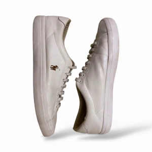 Polo Ralph Lauren skor - Snygga vita sneakers från Polo Ralph Lauren med klassisk rund tå och platt sula. Perfekta för dig som gillar enkel och clean stil.