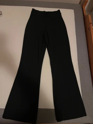 Svarta bootcut byxor med hög midja - Snygga svarta bootcut byxor med hög midja och raka ben. Materialet är mjukt och har lite stretch, vilket gör dem bekväma att bära. Perfekta för dig som gillar en stilren och trendig look med markerad siluett.