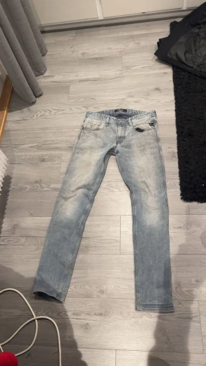 Replay ljusgrå anbass - Säljer ett par ljusgrå Replay jeans med snyggt slitna detaljer och klassisk femficksdesign. Modellen har raka ben och normal passform, med coola bakfickor och diskret Replay-logga. Perfekt för dig som gillar en avslappnad streetstil. 32/34
