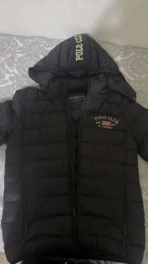 Svart pufferjacka Polo Club XS - Svart pufferjacka från Polo Club i storlek XS. Jackan har huva med Polo Club-tryck, broderade loggor på bröstet och ärmen, samt två fickor med dragkedja. Perfekt för kalla dagar och har en stilren look med quiltad design.