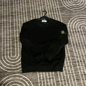 Svart Stone Island sweatshirt M - Svart sweatshirt från Stone Island i storlek M. Klassisk rund hals och ribbade muddar. Ikonisk logotyp-patch på vänster ärm. Perfekt för dig som gillar streetwear och vill ha en clean look. Fraktar samma dag😊