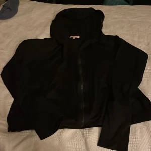 Svart träningtröja med dragkedja och huva från Filippa K Soft Sport - Svart träning tröja  från Filippa K Soft Sport i storlek S. Jackan har huva, hel dragkedja framtill och är tillverkad i ett lätt, mjukt polyestermaterial. Perfekt för chill dagar eller när du vill ha en clean look. Enkel design utan mönster eller extra detaljer.Så snygg och härlig kvalitet.