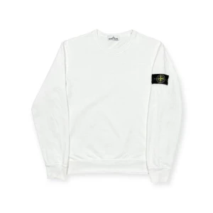 Vit sweatshirt från Stone Island - Vit långärmad sweatshirt från Stone Island med klassisk rund hals och ikonisk svart patch med logga på vänster ärm. Tröjan är tillverkad i mjuk bomull och har ribbade muddar vid ärmslut och nederkant. Perfekt för dig som gillar clean och stilren streetwear.
