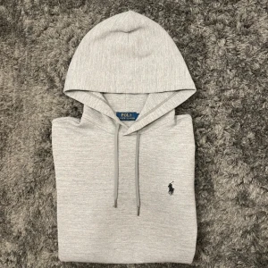 Grå hoodie från Polo Ralph Lauren - Hej! Säljer en grå Ralph Lauren Hoodie med svart pony. På en av ärmarna har den ett väldigt litet hål som knappt syns, samt en liten svart fläck. Dessutom finns det ett mycket litet hål vid bröstet, se bild. Utöver detta är den mycket fin. Den är i storlek S. Hör av er vid frågor!