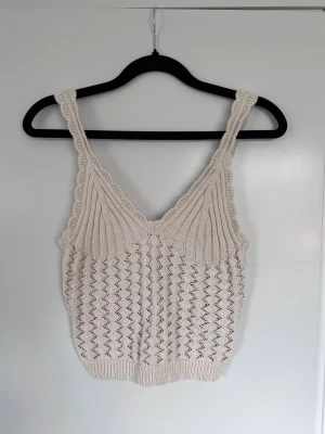 Beige stickad linnetopp med v-ringning, H&M storlek S - Superfin beige stickad linnetopp med v-ringning. Snyggt hålmönster och ribbade kanter. Perfekt för varma dagar och att styla med jeans eller kjol.