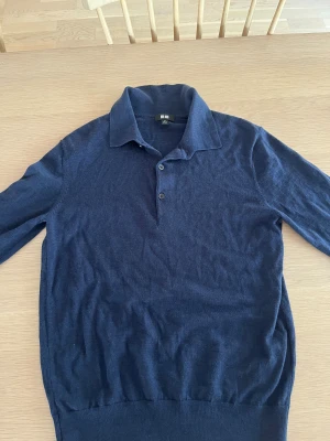 Mörkblå pikétröja från Uniqlo XS - Snygg mörkblå pikétröja från Uniqlo i storlek XS. Tröjan har klassisk krage, två knappar och är långärmad. Tillverkad i mjukt stickat material som känns skönt mot huden. Perfekt för dig som gillar stilren och enkel design.