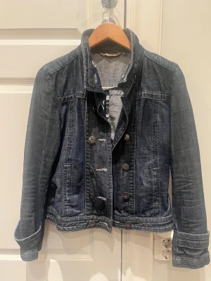 Mörkblå jeansjacka Tommy Hilfiger - Snygg mörkblå jeansjacka från Tommy Hilfiger med klassisk krage och dubbla knapprader framtill. Jackan har långa ärmar, coola detaljer vid muddar och en schysst tvättad denimlook. Perfekt för dig som vill ha en tidlös och trendig jacka i garderoben.