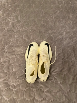 Nike fotbollsskor i ljusgult och svart - Säljer ett par snygga Nike fotbollsskor i ljusgul färg med svarta detaljer och stor logga på sidan. Skorna har snörning och platt sula med dobbar för gräsplan. Tillverkade i syntetmaterial med rund tå och sportig design.