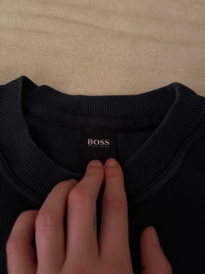 Mörkblå sweatshirt från Hugo Boss - Snygg mörkblå sweatshirt från Hugo Boss med stort BOSS-tryck på bröstet. Tröjan har rund hals, ribbade muddar och långa ärmar. Perfekt för dig som gillar stilrena och klassiska märkesplagg. Materialet känns mjukt och skönt mot huden.