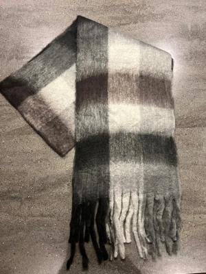 Halsduk - Supermjuk och bred halsduk som verkligen liknar acne studios, med rutigt mönster i olika nyanser av grått, svart och vitt. Lång modell med tjocka, fluffiga fransar i ändarna. Perfekt att svepa runt halsen för extra värme och stil under kyliga dagar.