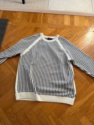 Vit och marinblå stickad tröja Holebrook - Säljer en stickad tröja från Holebrook Sweden i storlek 2XL. Tröjan är vit med marinblå rutor, har rund hals och långa ärmar. Ribbstickade muddar vid hals, ärmslut och nederkant. Perfekt för dig som gillar klassisk stil med lite edge.
