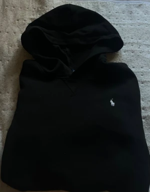 Svart hoodie från Polo Ralph Lauren - Svart hoodie från Polo Ralph Lauren i storlek XL (barn storlek) med klassisk huva och broderad vit logga på bröstet. Tröjan är aldrig annvänd då den var för liten för mig.