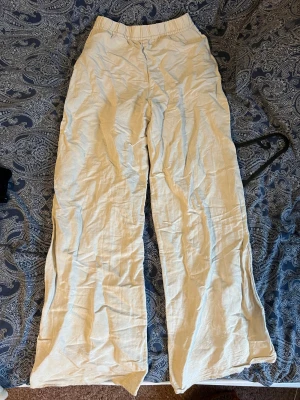 Beiga vida linnebyxor med snörning - Säljer ett par beiga linnebyxor med bred passform och elastisk midja med snörning. Byxorna är lätta och luftiga, perfekta för varmare dagar. De har en avslappnad stil och är tillverkade i linne för en skön känsla.