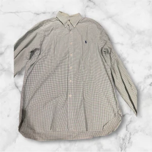 Rutig skjorta från Ralph Lauren - Klassisk rutig skjorta från Ralph Lauren i ljusa toner med diskret broderad logga på bröstet. Skjortan har lång ärm, knappar framtill och en snygg krage. Perfekt för dig som gillar stilrena och tidlösa plagg.