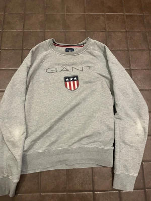 Grå sweatshirt från GANT  - Grå sweatshirt från gant. Armbågarna är ner nötta men ej hål, syns på bilden