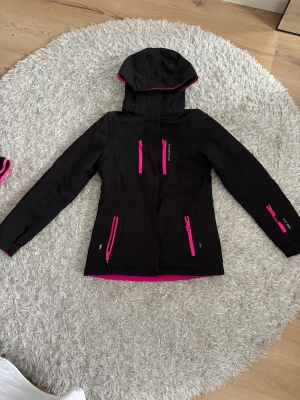 Svart Skidjacka - Supersnygg svart skidjacka med rosa detaljer från märket Swedemount. Jackan är endast använd vid 2 tillfällen så i mycket bra skick. Den är fodrad och har en ficka för liftkort på ena ärmen. Hör av er vid frågor💕🥰