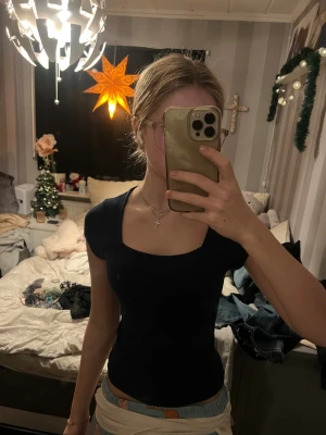 Marinblå topp med fyrkantig ringning från Gina Tricot - En marinblå , topp från Gina Tricot med korta ärmar och snygg fyrkantig ringning. Materialet är mjukt och stretchigt, troligen bomull med lite syntet. Perfekt för dig som gillar en enkel men stilren look. Passar dig som vill ha en topp som sitter snyggt och framhäver figuren.