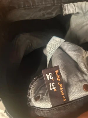 Svarta jeans från Nudie Jeans Co, W32 L34 - Svarta jeans från Nudie Jeans Co med klassisk femficksdesign och subtila sömdetaljer på bakfickorna. Jeansen har rak passform och är tillverkade i slitstarkt denimtyg. Perfekt för dig som gillar stilrena och tidlösa jeans.