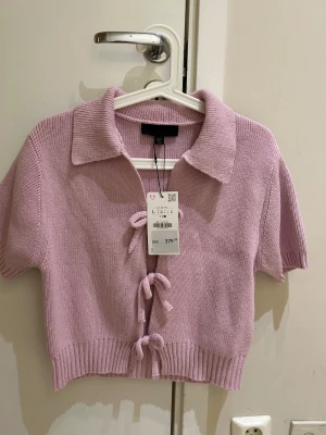  Ny Ljuslila stickad topp från Zara - Superfin ljuslila stickad topp från Zara med korta ärmar och krage. Toppen har croppad passform och snygga snörningsdetaljer framtill. Perfekt för dig som gillar trendiga och bekväma plagg med lite extra attityd. Passar til S och M i storlek 