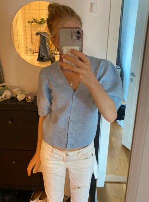 Ljusblå stickad kofta från Gina Tricot - Supersöt ljusblå stickad kofta från Gina Tricot med korta ärmar och v-ringning. Koftan har knappar framtill och ribbade muddar vid ärmslut och nederkant. Perfekt att slänga på över ett linne eller t-shirt för en chill look. Tröjan är bara testat aldrig använd så den är som ny!!