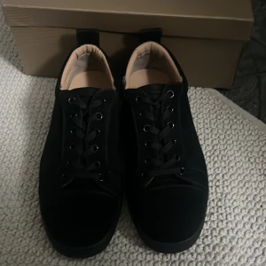 Svarta sneakers från Christian Louboutin - Snygga svarta sneakers från Christian Louboutin med klassisk röd sula. Skorna har rund tå, snörning och är tillverkade i skinn med en matt finish. Insidan är beige och de har en platt sula som ger en clean och modern look. Använda ett par gånger. Box ingår ej.