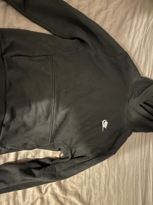 Svart Nike hoodie storlek 158 - Svart hoodie från Nike i storlek 158 med klassisk logga broderad i vitt på bröstet. Tröjan har huva, lång ärm och stor magficka framtill. Materialet är mjukt och känns som bomull med insida i fleece för extra komfort. Perfekt för chill eller träning.