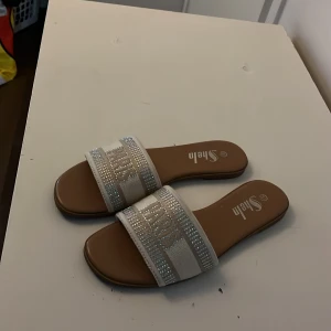 Vita sandaler med strass och text - Snygga vita sandaler från SheIn med bred rem dekorerad med glittrande strass och texten 'PARIS'. Platt sula och öppen tå ger en chill vibe. Perfekta för sommardagar när du vill sticka ut lite extra.