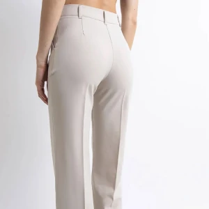 Beiga kostymbyxor Madlady - Snygga beiga kostymbyxor med hög midja och raka ben. Byxorna har pressveck framtill och  bälteshällor. Perfekta för en clean och stilren look. Dem är regular i längden