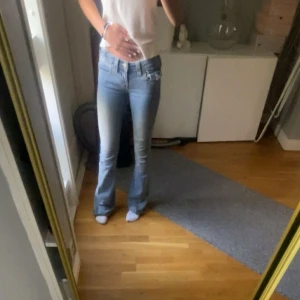 True Religion Joey Low Rise Flare jeans - Säljer ett par ljusblå True Religion Joey jeans med låg midja och utsvängda ben. Klassisk femficksmodell med snygga detaljer på bakfickorna och slitningar. Jeansen är i stretchigt denim och har en riktigt schysst flare-passform.