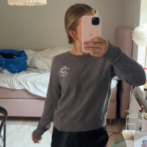 Grå sweatshirt från Hollister - Mysig grå sweatshirt från Hollister med rund halsringning och vit logga på bröstet. Tröjan har långa ärmar och ribbade muddar vid ärmslut och nederkant. Perfekt för chill dagar eller när du vill vara bekväm.