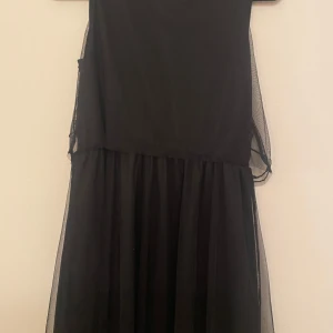 Svart paljettklänning från KappAhl - Supersnygg svart långklänning från KappAhl med transparent mesh och glittriga paljettdetaljer på överdelen. Klänningen har ärmlös design och ett elegant mönster framtill. Perfekt för dig som vill sticka ut med en klassisk look.