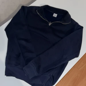 Mörkblå half zip tröja från Zara - Mörkblå långärmad tröja från Zara med half zip-dragkedja vid halsen. Tröjan har en klassisk, enkel design och är gjord i mjuk bomullsmix som känns skön mot huden. Perfekt för lager-på-lager och chill dagar.