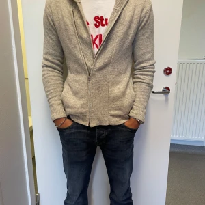 Ljusgrå kofta från Armani Exchange - Snygg ljusgrå kofta från Armani Exchange med dragkedja framtill. Koftan är stickad i mjukt material och har långärmad design med ribbade muddar. Perfekt för lager-på-lager och enkel att matcha med jeans eller chinos.