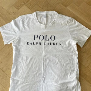 Vit t-shirt från Polo Ralph Lauren - Vit t-shirt från Polo Ralph Lauren med klassisk rund hals och stor logotyp-print på bröstet. Modellen är kortärmad och har en clean, enkel look. Tillverkad i mjuk 100% bomull som känns skön mot huden. Perfekt för dig som gillar stilrena och tidlösa plagg. Pris går att diskutera. Självklart äkta!