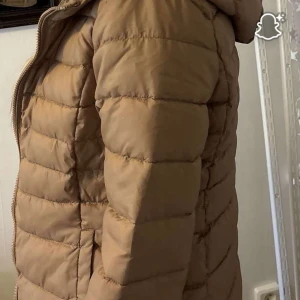 Beige pufferjacka med dragkedja - Säljer en beige pufferjacka med huva och dragkedja framtill. Den är från nelly och passar som höst och vinterjacka