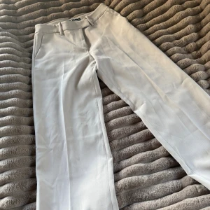 Beiga kostymbyxor från BikBok - Snygga beiga kostymbyxor från BikBok i rak modell. Byxorna har hällor för bälte, diskreta fickor och stängs med dragkedja och knapp. Perfekta för en clean och stilren look.