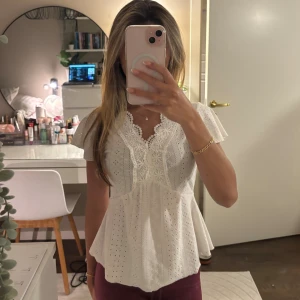 Vit spetsblus med volangärm - Supersöt vit blus med broderade spetsdetaljer och v-ringning. Blusen har korta volangärmar och är med hålmönster. Den har en lätt utsvängd passform som ger en romantisk vibe och passar perfekt till jeans eller kjol. Hör av dig om du har några frågor! 🫶🏼💕