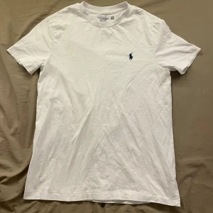 Vit t-shirt från Ralph Lauren - Klassisk vit t-shirt från Ralph Lauren med broderad marinblå logga på bröstet. Använt bara en gång och den är helt ren och i ett mycket bra skick. Storlek S, män. Skickar inom 1-3 dagar och pris kan diskuteras