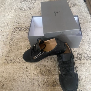 Svarta sneakers från Giuseppe Zanotti - Säljer ett par svarta sneakers från Giuseppe Zanotti i modellen Microstar-Trend. Skorna har glittrig finish, snörning och silverfärgade dragkedjor på sidorna. Insidan är beige och sulan är svart. Riktigt snygga och unika sneakers för dig som vill sticka ut.