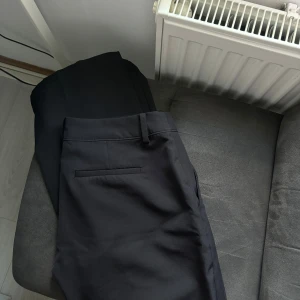 Svarta kostymbyxor från BikBok - Klassiska svarta kostymbyxor från BikBok i storlek 36. Byxorna har hällor för bälte, diskreta fickor bak och stängs med dragkedja och hake. Perfekta för en clean och stilren look, passar till allt och är lätta att matcha.