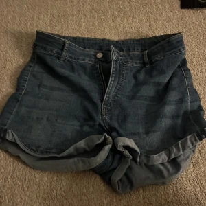 Blå jeansshorts från Divided - Snygga blå jeansshorts från Divided i klassisk denim med uppvikta benslut och femficksmodell. Shortsen har normal passform och stängs med knapp och dragkedja. Perfekta för sommardagar och enkla att matcha med allt. Säljer för att dom är för stora. Skicket är väldigt bra och dom är snygga på. 