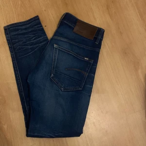 G-Star Raw 3301 Slim jeans blå 28/30 - Snygga mörkblå jeans från G-Star Raw, modell 3301 Slim. Jeansen har klassisk femficksdesign, smal passform och coola slitningar på låren. Tillverkade i jeansmaterial med snygga kontrastsömmar och läderpatch bak i midjan. Nypris 1199.